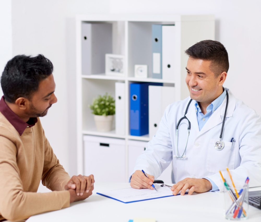 medicine, healthcare and people concept - happy doctor with clipboard and young male patient meeting at hospital